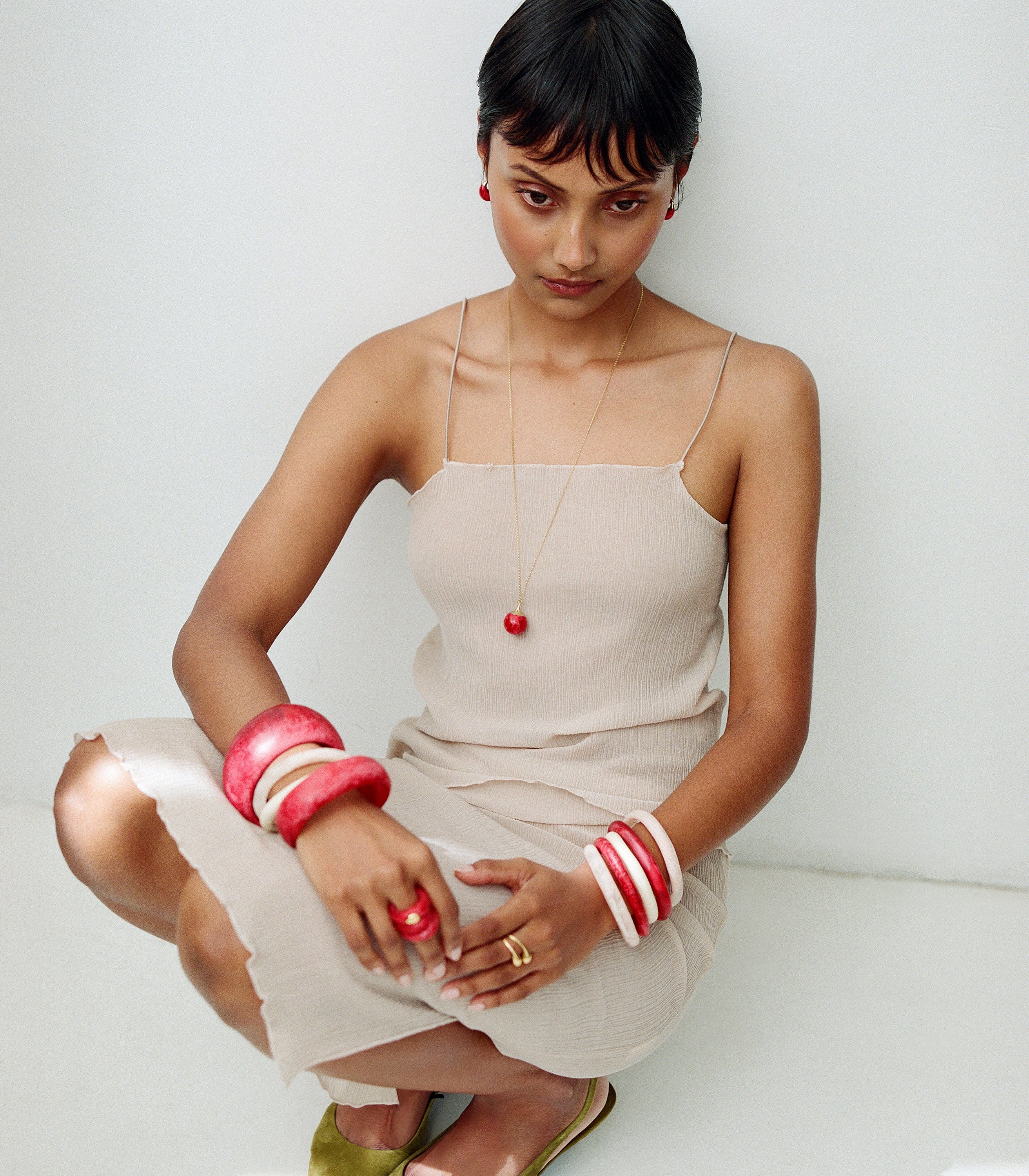 Model wearing beige dress with pink toned resin bangles and rings with brass accent rings and pendant