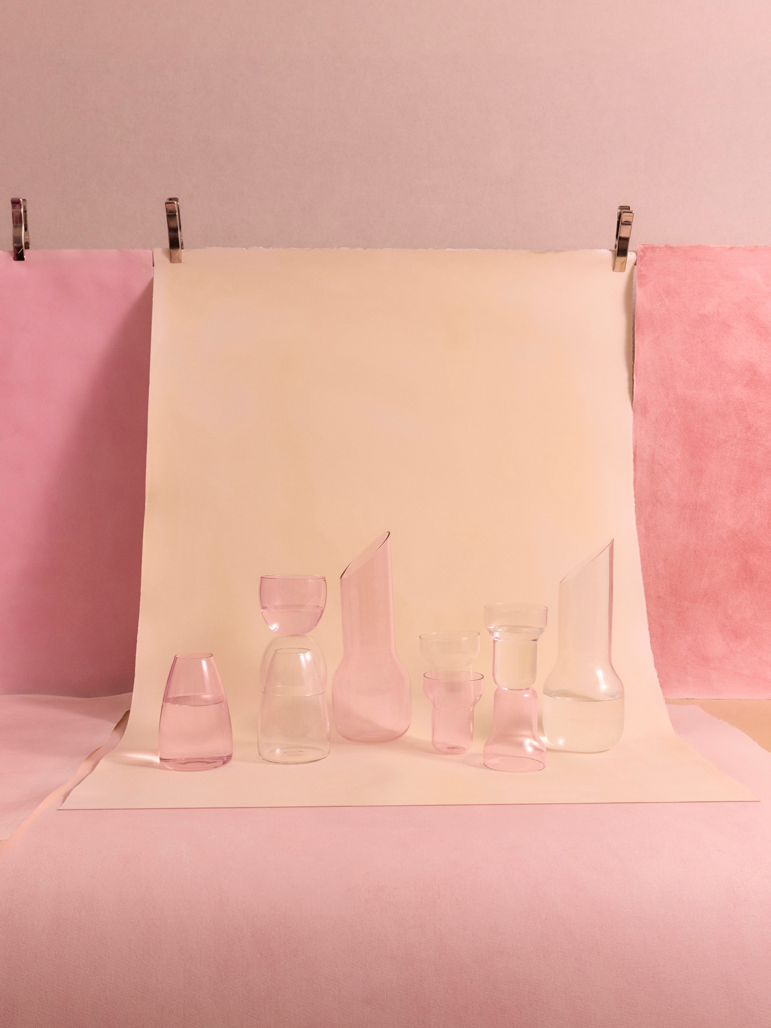 Variety of pink and clear decanters, carafes, and drinking glasses on a beige and pink backdrop