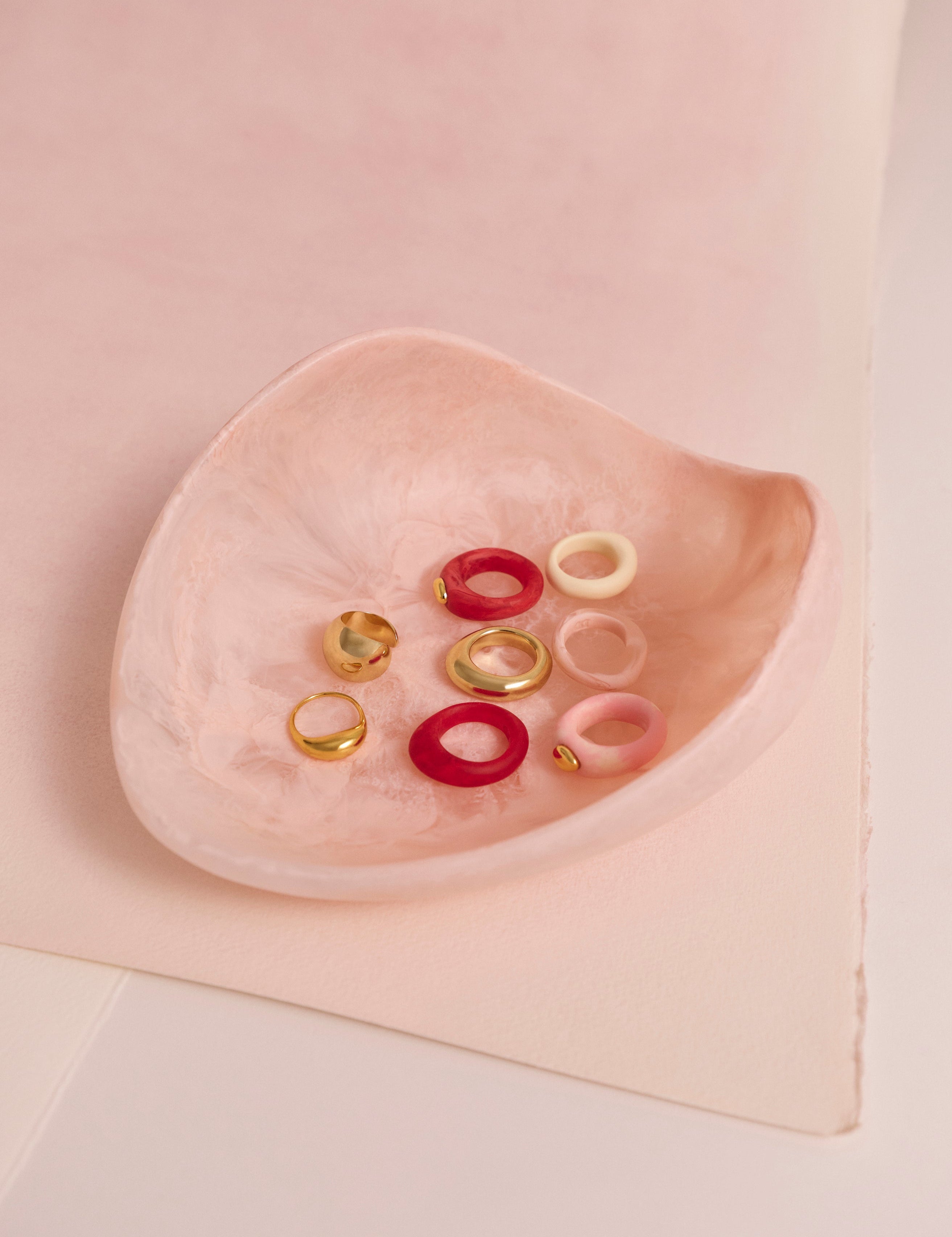 A pink resin bowl holding a variety of brass and pink resin rings
