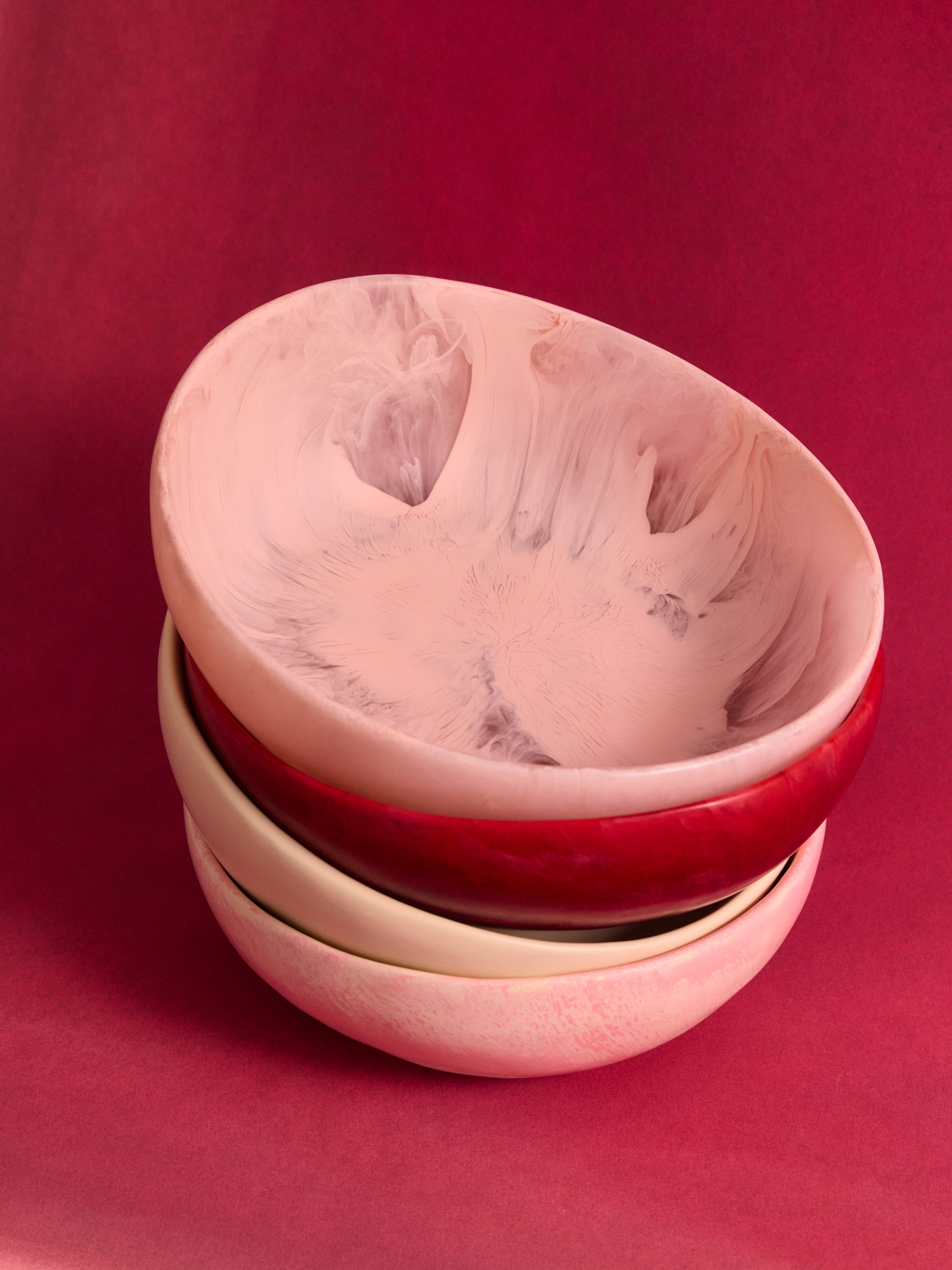 Stack of resin salad bowls in pinks and cream on a pink backdrop