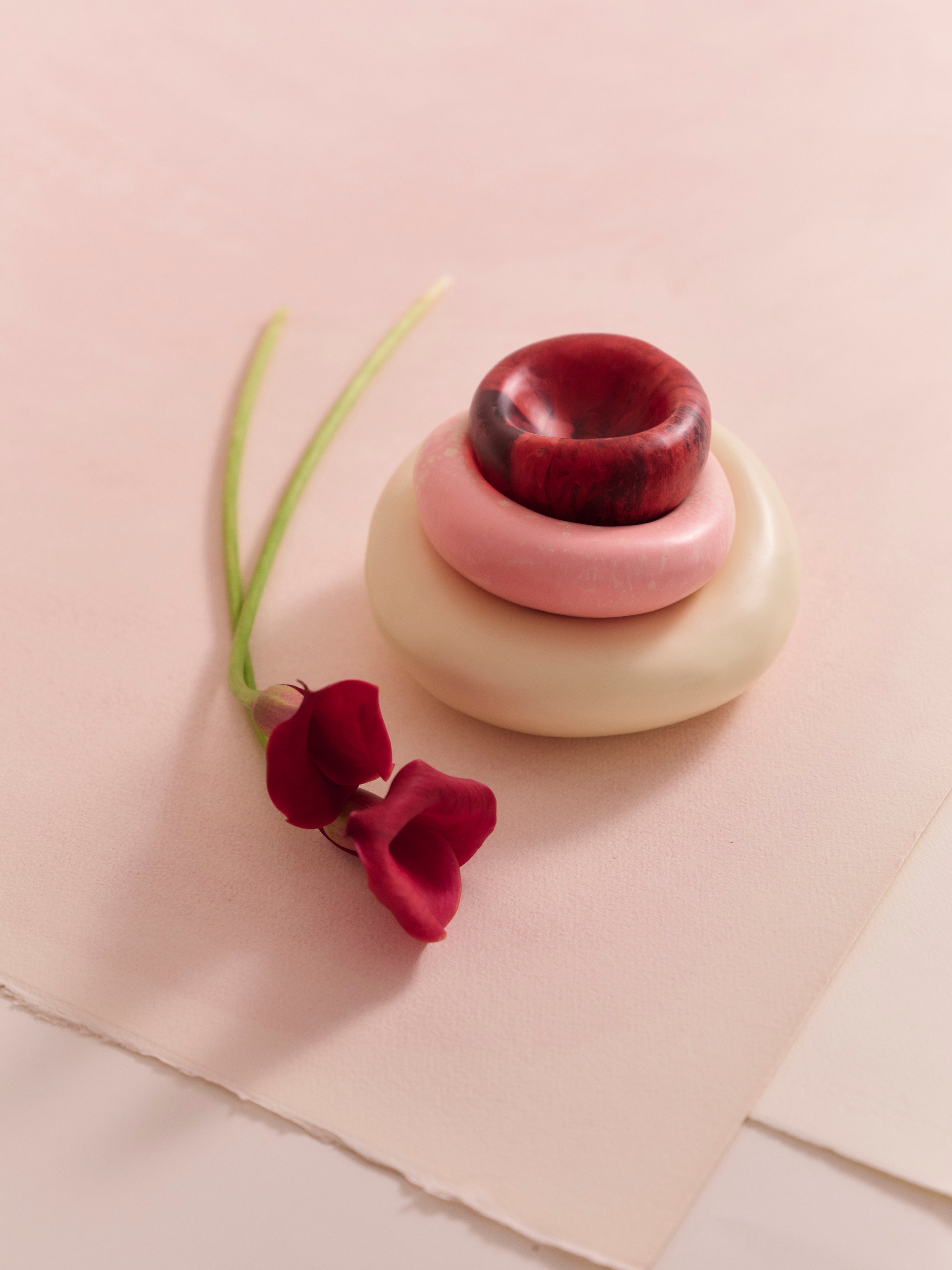 Stack of resin dishes accompanied by floral stem on a beige backdrop