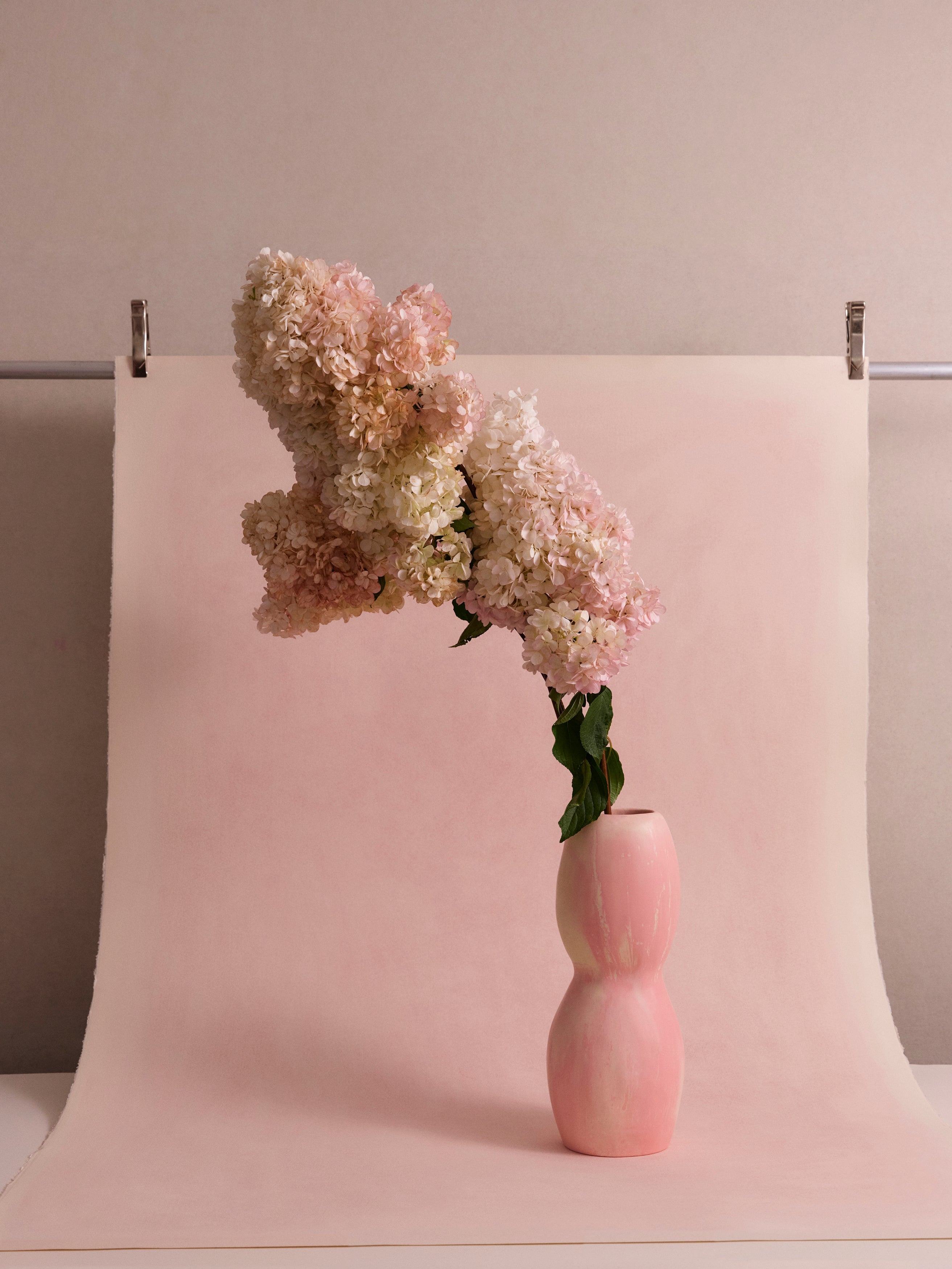 Tall pink and cream marbled resin vase with large floral arrangement on a light pink backdrop
