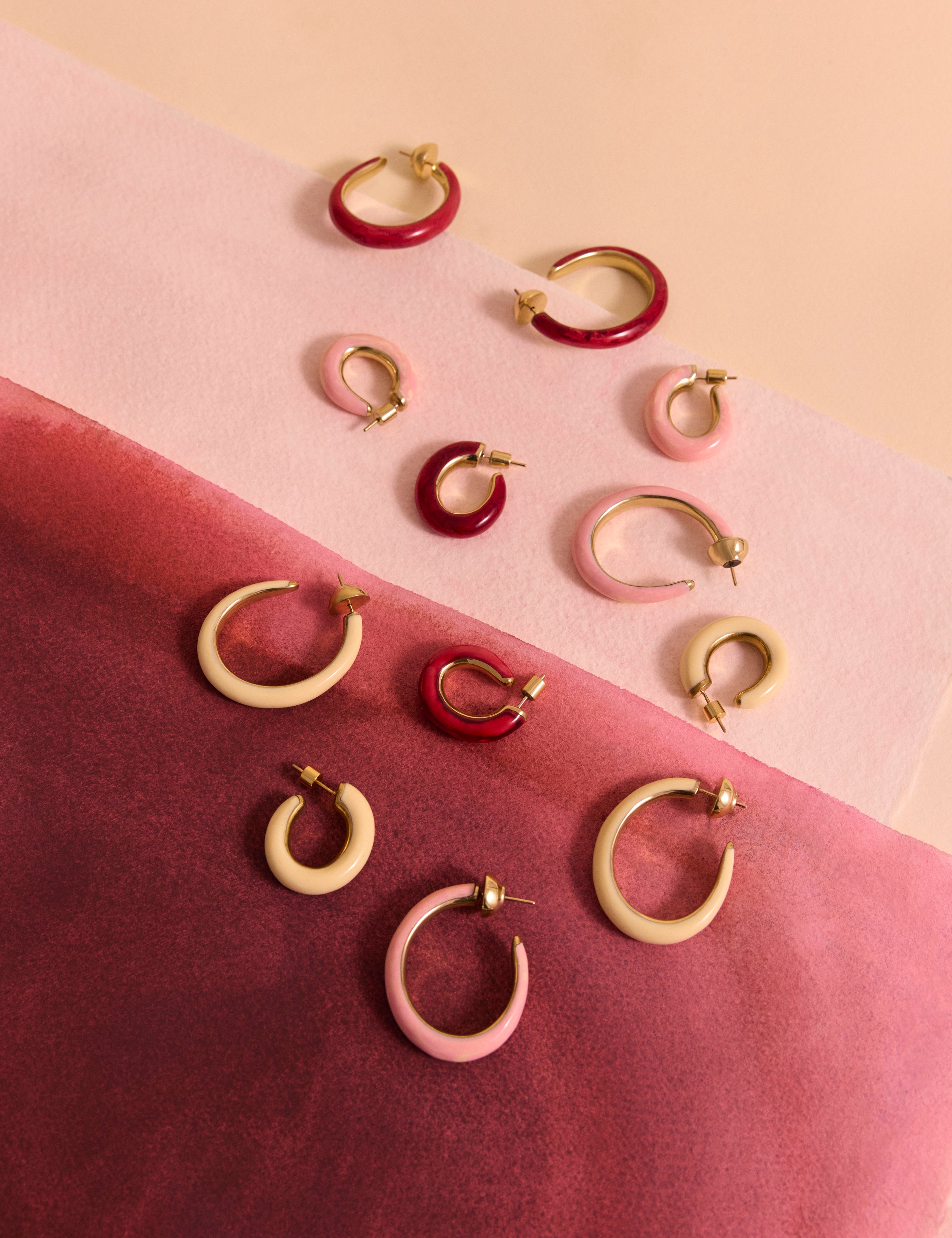 Variety of resin and brass oval hoop earrings on pink backdrop
